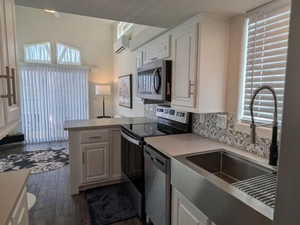 Kitchen featuring a wall unit AC, appliances with stainless steel finishes, a peninsula, a sink, and backsplash