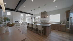 Kitchen with light wood-style flooring, a kitchen breakfast bar, decorative backsplash, a center island with sink, and pendant lighting