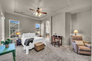 Bedroom with light carpet, visible vents, a tray ceiling, and arched walkways