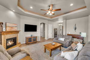 Living area with arched walkways, a raised ceiling, a fireplace, and baseboards