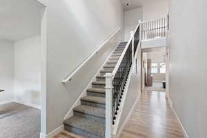 Stairs with a towering ceiling, baseboards, and wood finished floors