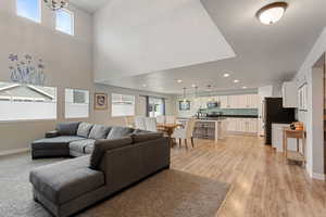 Living room with recessed lighting, light wood-type flooring, a high ceiling, and baseboards