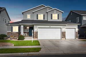 View of front of home with stone siding, a shingled roof, concrete driveway, and stucco siding