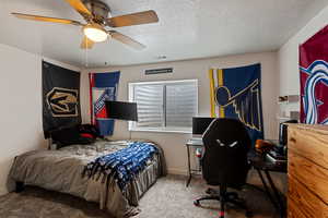 Bedroom featuring a textured ceiling, carpet floors, visible vents, a ceiling fan, and baseboards