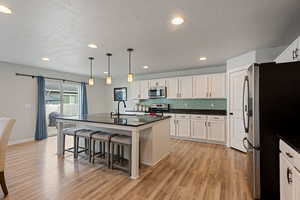 Kitchen with stainless steel appliances, dark countertops, a kitchen island with sink, and white cabinets