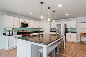 Kitchen with appliances with stainless steel finishes, white cabinetry, a sink, and an island with sink