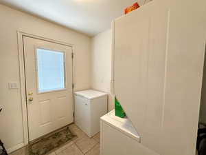 Laundry area with stacked washer and clothes dryer and light tile patterned floors