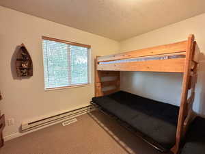 Bedroom with carpet floors, a textured ceiling, and baseboard heating