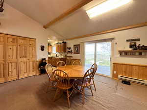 Dining area featuring lofted ceiling with beams, wooden walls, light colored carpet, and baseboard heating