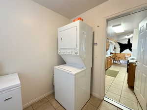 Laundry area with stacked washer and dryer and light tile patterned floors