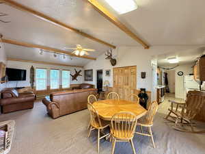 Carpeted dining area featuring lofted ceiling with beams and ceiling fan