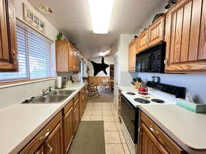 Kitchen featuring electric stove, light tile patterned flooring, sink, and a textured ceiling