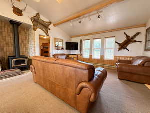 Living room with rail lighting, vaulted ceiling with beams, a wood stove, carpet, and a baseboard heating unit