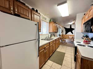 Kitchen with sink, light tile patterned floors, range with electric cooktop, a textured ceiling, and white fridge