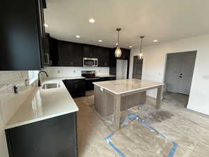 Kitchen with decorative backsplash, a sink, dark cabinets, stainless steel appliances, and recessed lighting