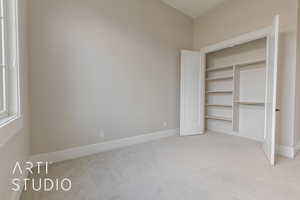 Unfurnished bedroom with a closet, light carpet, and baseboards