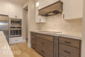 Kitchen featuring stainless steel appliances, light countertops, custom range hood, light wood-style floors, and white cabinets