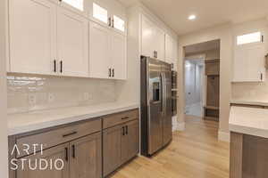 Kitchen with light stone counters, white cabinetry, appliances with stainless steel finishes, light wood-type flooring, and glass insert cabinets