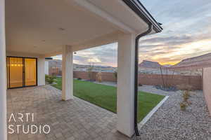 Patio terrace at dusk with a fenced backyard, a mountain view, and a lawn