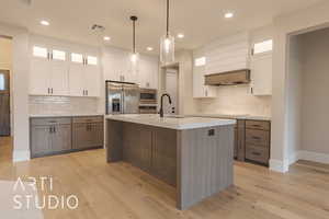 Kitchen featuring glass insert cabinets, stainless steel appliances, white cabinets, light countertops, and a center island with sink