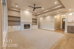 Unfurnished living room featuring visible vents, a ceiling fan, light wood-type flooring, a tray ceiling, and a tiled fireplace