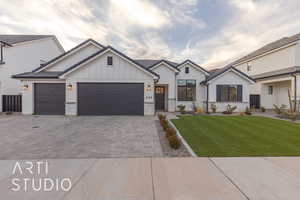 Modern farmhouse with an attached garage, decorative driveway, board and batten siding, and a front yard