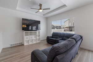 Living room with a raised ceiling, visible vents, and light wood-style floors