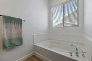 Bathroom with wood finished floors, a garden tub, and baseboards