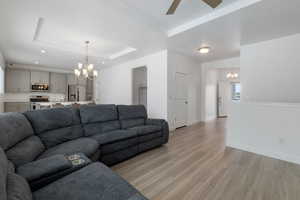 Living area with recessed lighting, ceiling fan with notable chandelier, baseboards, light wood-style floors, and a tray ceiling