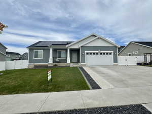 Single story home with a porch, a gate, roof mounted solar panels, driveway, and an attached garage