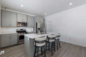 Kitchen featuring gray cabinetry, appliances with stainless steel finishes, a kitchen island with sink, a sink, and a kitchen bar