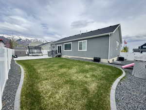 Rear view of house with a trampoline, a yard, stucco siding, central AC unit, and a fenced backyard