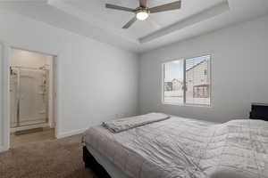 Carpeted bedroom featuring ensuite bath, baseboards, a tray ceiling, and a ceiling fan