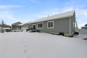 Snow covered back of property featuring central AC, a trampoline, fence, and stucco siding