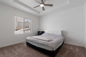 Bedroom with a ceiling fan, a raised ceiling, dark carpet, and baseboards