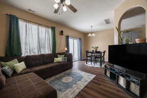 Living room featuring dark wood-style floors, a textured ceiling, ceiling fan with notable chandelier, and visible vents