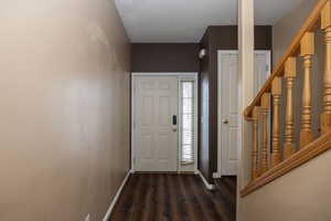 Entryway with stairs, a textured ceiling, dark wood-style floors, and baseboards