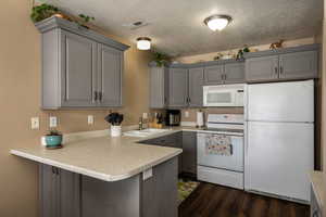 Kitchen featuring light countertops, white appliances, a peninsula, and gray cabinetry