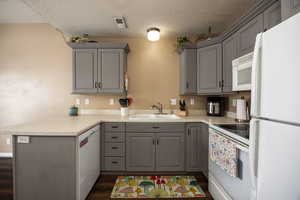 Kitchen with a peninsula, white appliances, a sink, light countertops, and gray cabinets