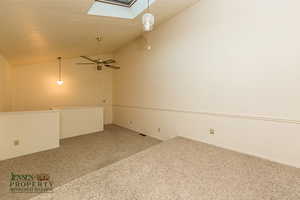 Carpeted empty room with a textured ceiling, vaulted ceiling with skylight, and a ceiling fan