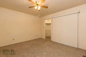 Unfurnished bedroom featuring a textured ceiling, carpet flooring, a ceiling fan, a spacious closet, and a closet