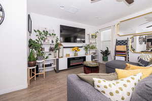 Living room featuring visible vents, a ceiling fan, a glass covered fireplace, wood finished floors, and baseboards