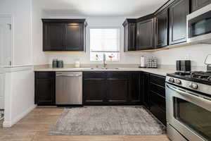 Kitchen with light countertops, light wood-style flooring, appliances with stainless steel finishes, a sink, and dark cabinetry