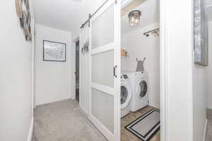 Laundry room with light carpet, laundry area, a barn door, baseboards, and separate washer and dryer