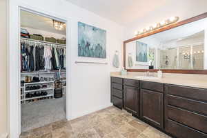 Primary bath with vanity, baseboards, a shower stall, stone finish floor, and a walk in closet