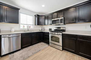 Kitchen with recessed lighting, stainless steel appliances, a sink, light countertops, and light wood finished floors