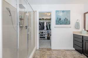 Primary bathroom featuring a stall shower, baseboards, stone finish flooring, a spacious closet, and vanity