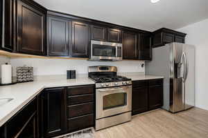 Kitchen featuring light wood-style floors, appliances with stainless steel finishes, light countertops, and dark brown cabinets