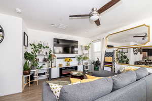 Living room featuring a ceiling fan, a glass covered fireplace, a textured ceiling, wood finished floors, and baseboards