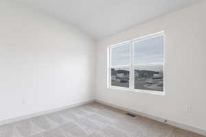 Empty room with carpet floors, lofted ceiling, visible vents, and baseboards